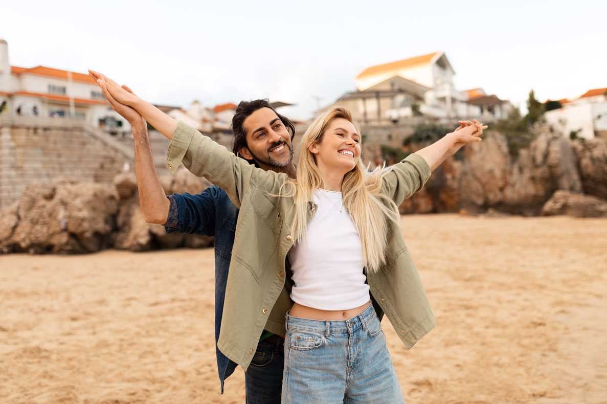 Casal feliz curtindo um dia ensolarado de praia com os braços estendidos