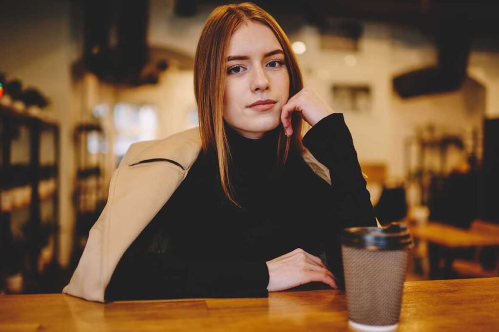 Mulher calma sentada á mesa de um café com um copo á frente