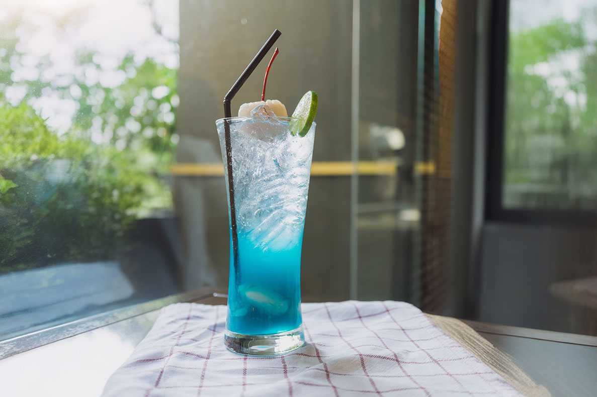 copo com refrigerante azul e gelo em cima de uma mesa